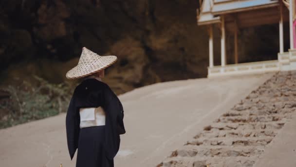 着物と竹の帽子を被った女性が 右に歩いて手の込んだ扇を振る — ストック動画