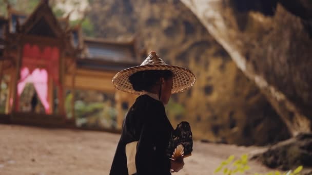 一位头戴和服 头戴竹帽的妇女挥动着她的手扇 走向洞里的库哈库鲁哈亭子 — 图库视频影像