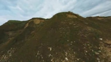 İnsansız hava aracı bir uçurumun tepesinden, deniz kıyısına doğru uçuyor.