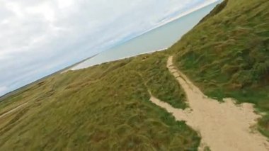 İHA 'nın deniz kenarındaki çimenli bir yamaçtan inen bir kadının üzerinde dönen manevralar yaparken çekilmiş görüntüleri.