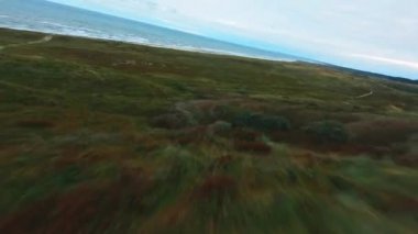 Bir tepeden deniz kenarındaki çimenli arazide yarışan bir dronun hava görüntüsü.
