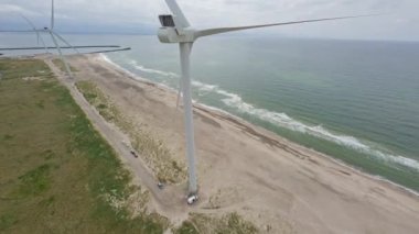 Aşağıdaki kumsala dalmadan önce rüzgar türbinine arkadan yaklaşan bir dronun hava görüntüsü.