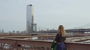 A video showing the back view of a woman at the Brooklyn bridge looking towards One Manhattan Square during daytime