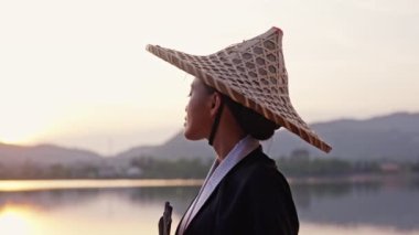 Kimono ve bambu şapkalı bir kadının Tayland 'da gün batımında Khao Tao Gölü Tapınağı' nda kameraya döndüğü orta boy bir yakın çekim.