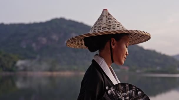 Woman Wearing Kimono Bamboo Hat Holding Hand Fan Looks Upward — Stock Video