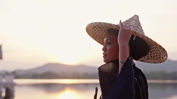 着物を着た女性が竹の帽子を調整すると タイのカオ タオ湖の寺院で日没を見るために進みます — ストック動画