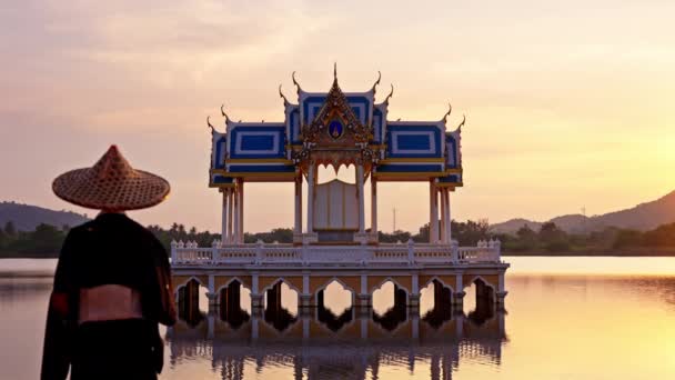 カオタオ湖の寺院の静止したショットと女性が横に見えるシーンに歩いて タイの日没時に飛んで鳥に焦点を当てる — ストック動画
