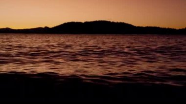 A video of the lake in Bariloche, Argentina showing the silhouette of the mountain from afar, and calm waters painted by the orange hue during sunrise