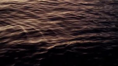 A close-up shot of the lake in Bariloche, Argentina showing its calm waters and ripples, painted by the orange hue during sunrise
