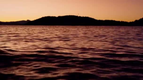 アルゼンチンのバリローチェの湖のビデオは遠くから山のシルエットを示し 日の出の間にオレンジ色の色合いで描かれた穏やかな水 — ストック動画