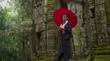 A full shot of a woman wearing a kimono, walking away from the ornate entrance of a temple in Cambodia during daytime