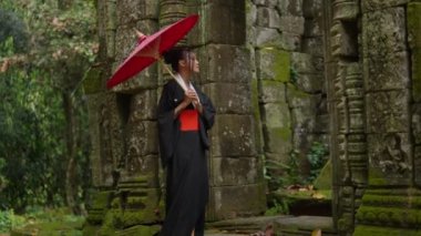 A full shot of a woman wearing a kimono, walking towards the ornate entrance of a temple in Cambodia during daytime