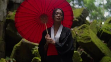 A medium shot of a woman wearing a kimono, looking around while walking inside the mossy temple ruins in Cambodia during daytime