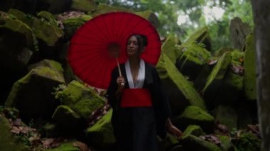 A video of a woman wearing a kimono, walking towards the camera at the mossy temple ruins during daytime in Cambodia