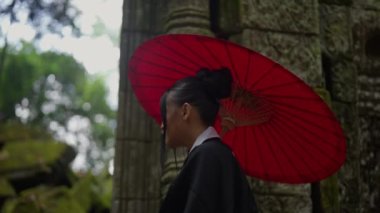 A medium close-up shot showing the side view and back view of a woman wearing a kimono, looking down while entering the mossy temple ruins in Cambodia during daytime