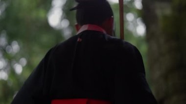 A medium close-up shot of a woman wearing a kimono, turning back and returning to the entrance of the mossy temple ruins during daytime in Cambodia