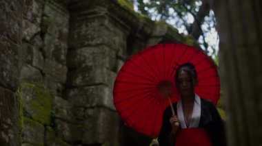 A video of a woman wearing a kimono, going out of the temple and heading to the forest during daytime in Cambodia