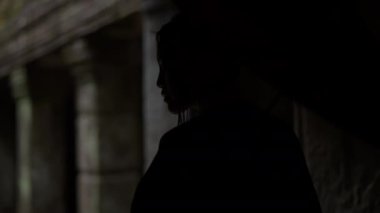 A tracking shot showing the back view of a woman walking inside the dim temple halls during in Cambodia