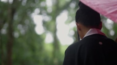 A tracking shot showing the back view of a woman wearing a kimono walking in the forest nearby the mossy temple ruins during daytime in Cambodia