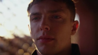 A close-up shot of a man staring straight ahead with bokeh effects and sun shining behind him