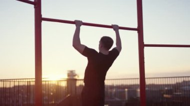 A video of a man doing pull-ups on the rooftop during sunset