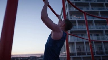 An arc shot of a man doing a calisthenic exercise called pull-ups on a rooftop during sunset