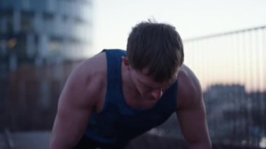 A close-up shot of a man at the rooftop doing push-ups during sunset