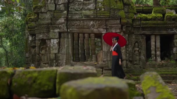 着物姿の女性の横顔が描かれたワイドショットで カンボジアの昼間は下枠の石で 苔むした寺院跡を歩く — ストック動画