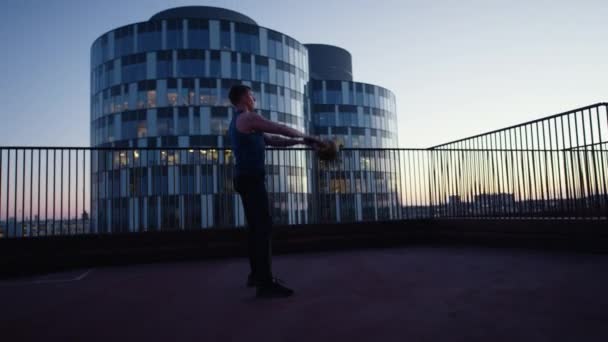 日没時に屋上でケトルベル前上げ運動をする男の側面図 — ストック動画