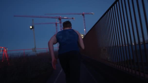 夕暮れ時に手すりの近くの屋上で速くジョギングをしている男の追跡ショット — ストック動画
