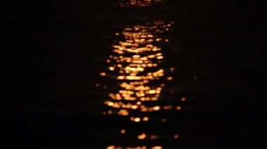 Video tilting upwards showing the sunset reflecting on the water and the stilts of the wooden jetty