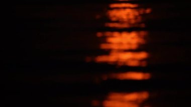 Close-up shot tilting upwards showing the reddish moonlight reflecting on water