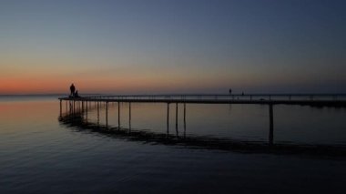 Silhouettes of people admiring the beautiful sunset on a seaside jetty