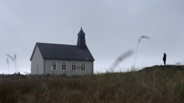 A low-angle long shot of a man standing outside the Strandarkirkja church during daytime