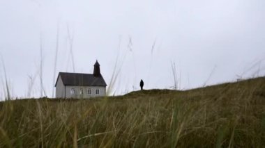 Time-lapse footage of a man standing outside the Strandarkirkja church while the wind blows over the grass
