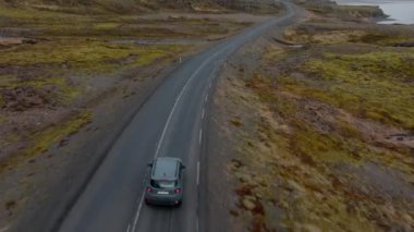 An aerial shot of a grey car venturing on a mountain pass road with a view of a river on the right side, in Iceland during daytime