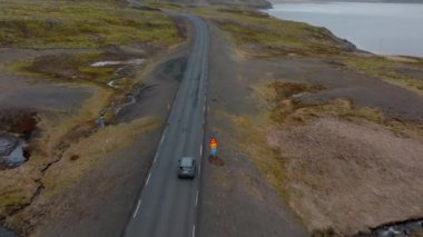 An aerial shot of a grey car venturing on a mountain pass road with a view of a river on the right side, in Iceland during daytime