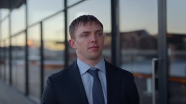 A medium close-up shot of a businessman, looking straight ahead, while walking outdoors along a glass facade during daytime