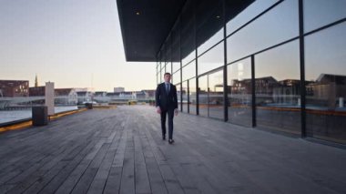 A full shot a businessman walking in a straight direction towards the camera with the Inner Harbour Bridge on the background