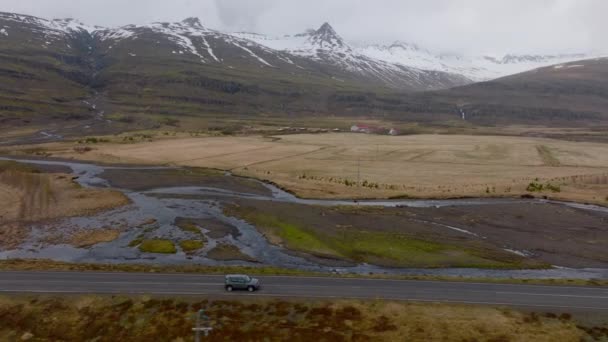 昼間のアイスランドの雪山を眺めながら山道を走る灰色の車のワイドショット — ストック動画