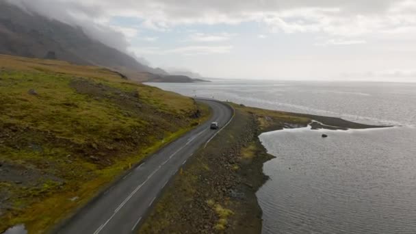 昼間にアイスランドの川岸近くの山道を走る灰色の車の空中撮影 — ストック動画