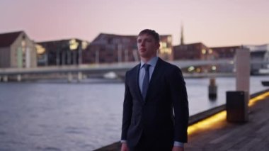 A medium shot of a businessman walking along the harbour during sunset