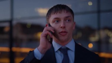 A close-up shot of a businessman holding on to his cellphone talking to someone while he is outdoors, in the city during daytime