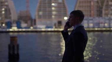A side view of a businessman talking to someone on his phone near the harbour during night time