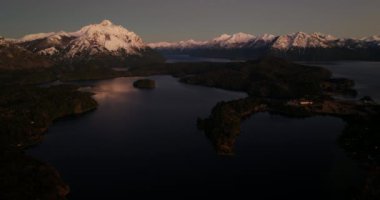 A wide drone flight panning from left to right, over the Nahuel Huapi lake with a view of Tronador mountain at Bariloche, Argentina during dawn