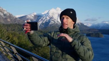 A video of a man recording himself with the Tronador mountain range behind during daytime