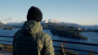 A video of a man in a green jacket walking towards the guardrails to see the view of the Bariloche landscape at Argentina during daytime