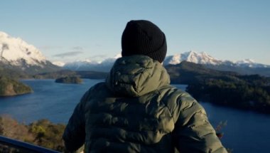 A video showing the back view of a man in a green jacket sightseeing the beautiful landscape of Nahuel Huapi Park at Bariloche, Argentina during daytime
