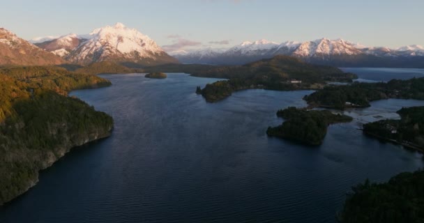日の出の間にアルゼンチンのバリローチェで太陽の光の山の範囲と緑豊かな緑の森を眺めながら ナウエル ハピ湖の上を移動する広い無人機の飛行 — ストック動画