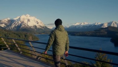 A video showing the back view of a man walking at the observation deck, sightseeing the landscape of Nahuel Huapi park at Bariloche, Argentina during daytime